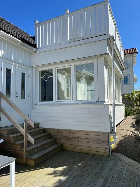 Trätrappa och trädäck vid entrén till en vit villa med burspråk