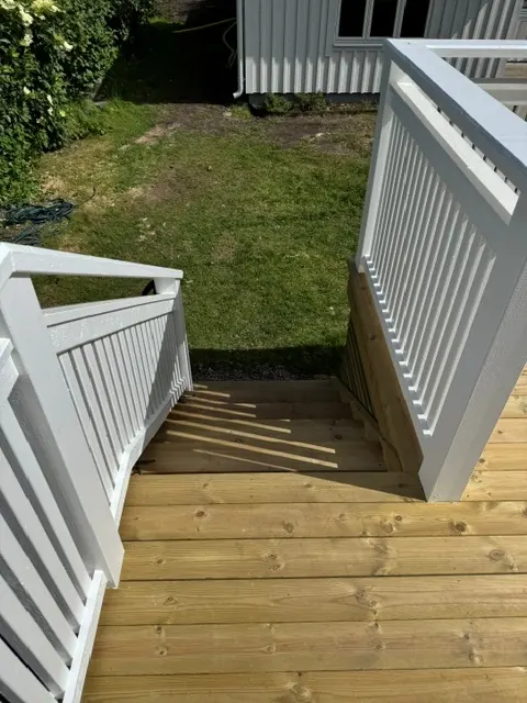 Trappa med vitmålat räcke ner från altanen till gräsmattan