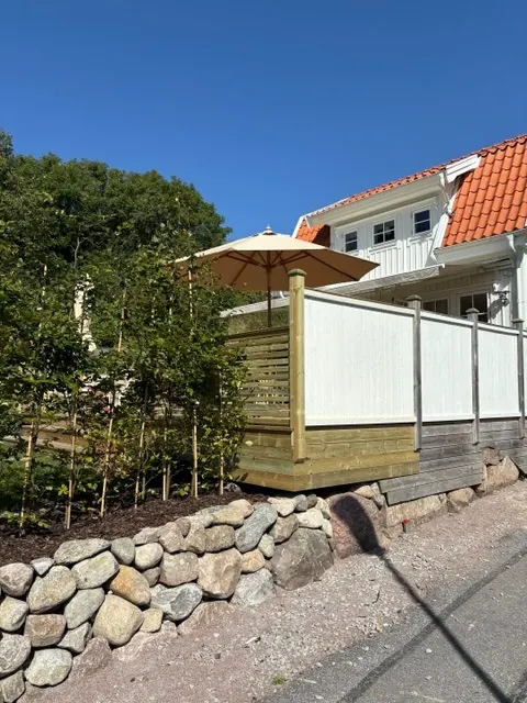 Altan med insynsskydd och parasoll sedd från gatan, stödmur i sten nedanför