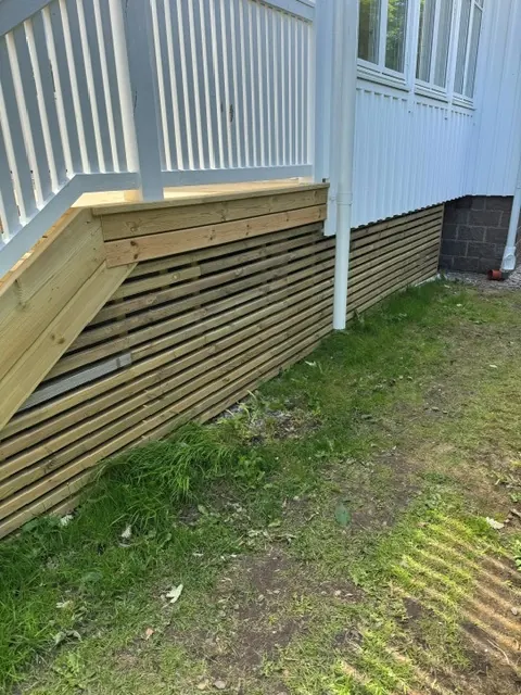 Inklädnad av liggande ribbor under en balkong med vitt räcke