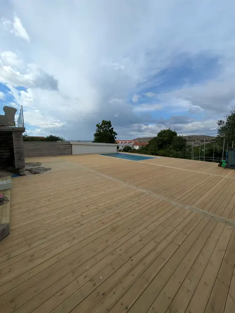 Trädäcket längs poolens långsida under molnig himmel